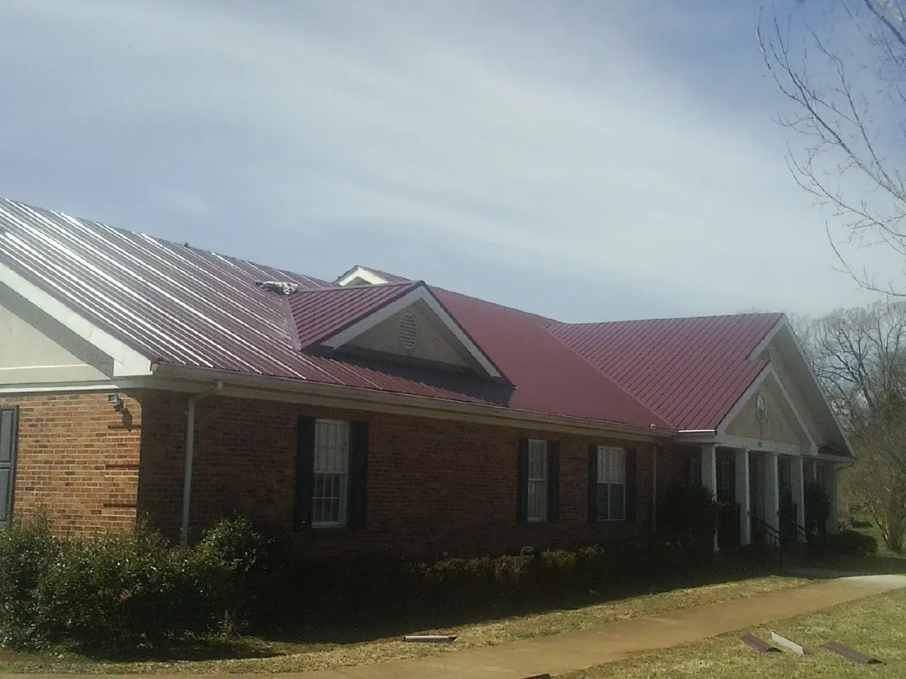 Red metal roof with gabled entries on a long brick building, from a Hail Damage Roof Repair job in Fruitland