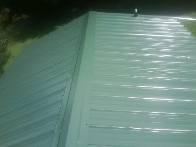 New green metal panels meeting at the ridge of a roof — Flat Roof Repair work by our crew in Fruitland